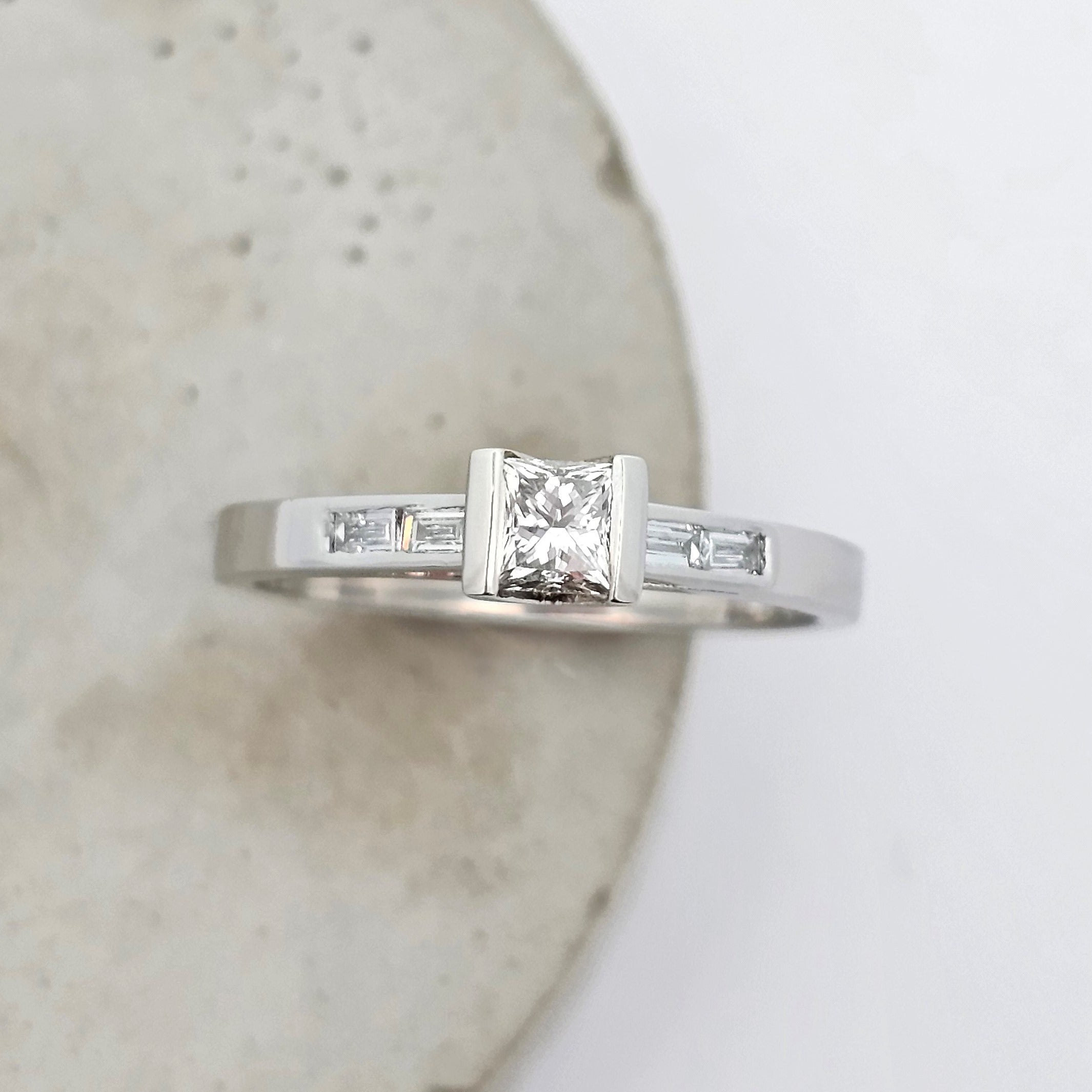 Platinum ladies engagement ring featuring an elevated semirub set princess cut diamond, stepping down to shoulders channels set with baguette diamonds.