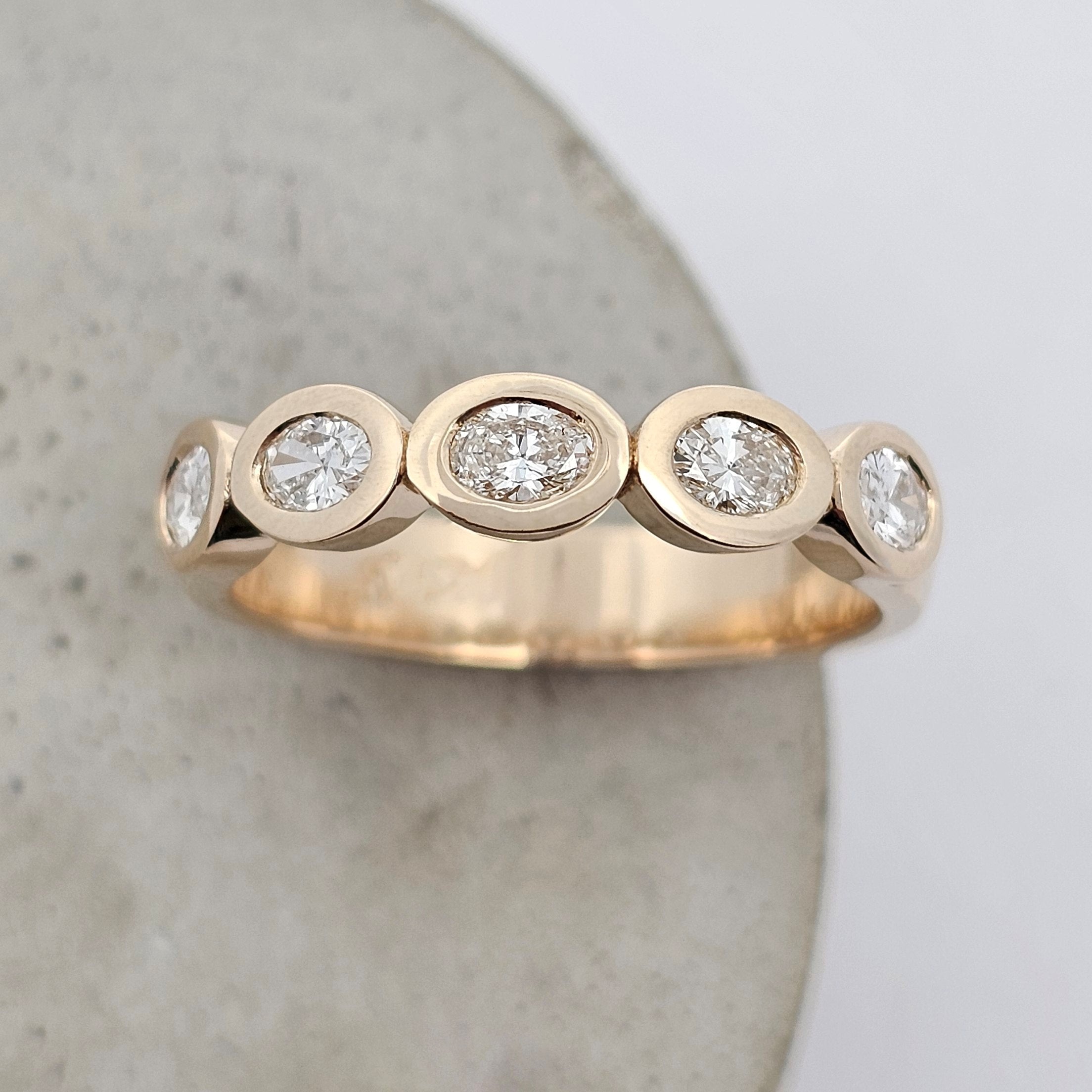 Diamond ring with oval diamonds individually framed in smooth golden bezels for a sleek, modern design.