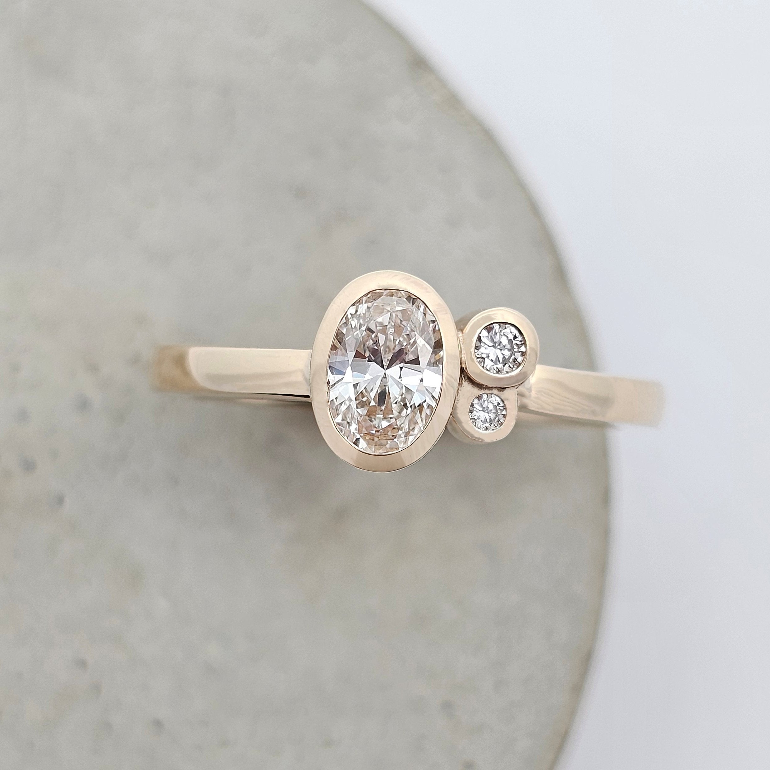 Yellow gold engagement ring featuring an oval diamond with two round side stones in a modern bezel setting