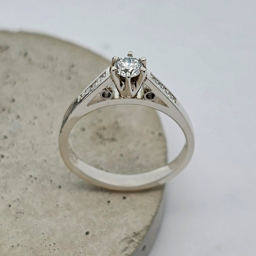 9ct white gold classic ladies engagement ring with a six claw set, bright white center diamond. The shoulders are channel set with a row of princess cut diamonds.