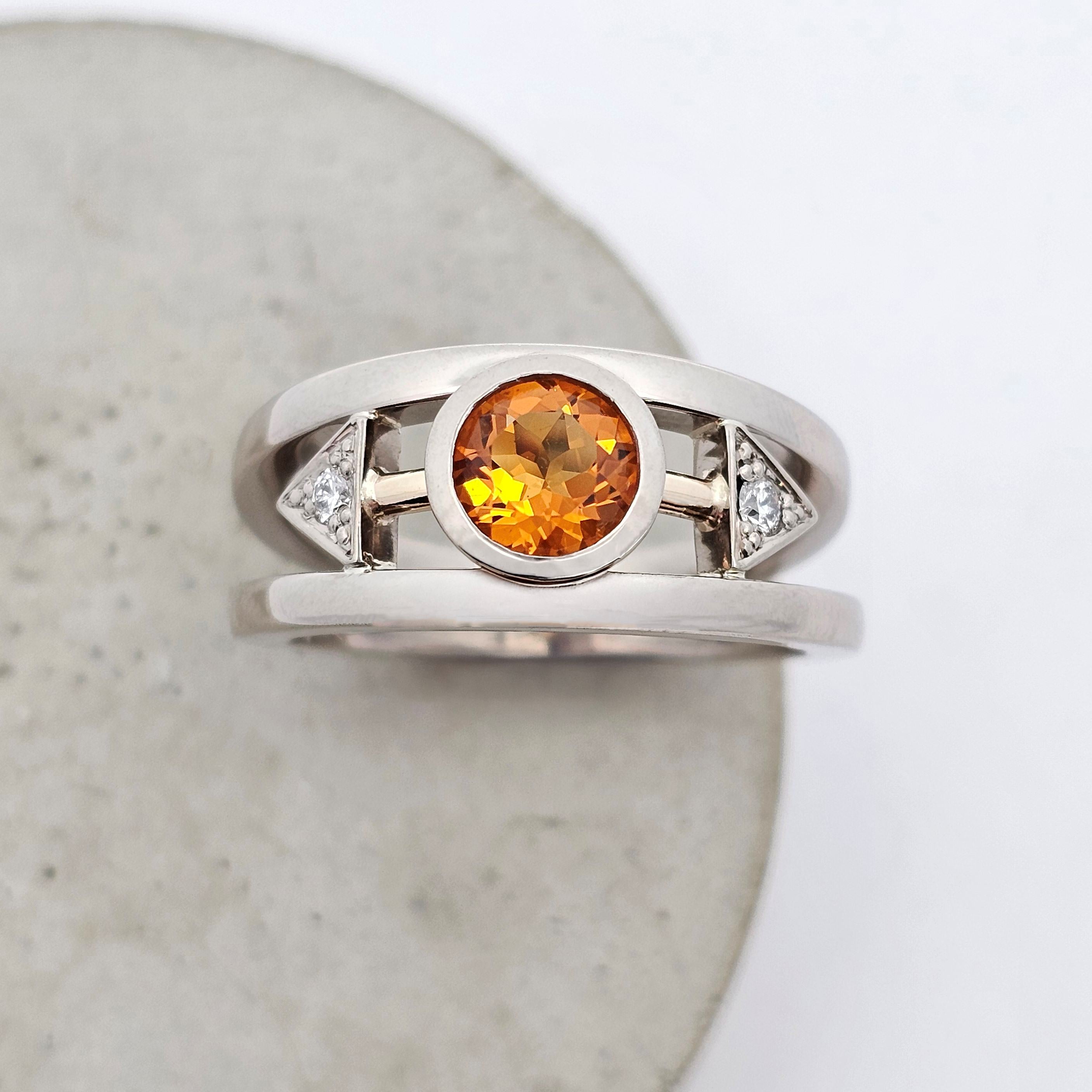 White gold citrine ring with a glowing golden-orange centre stone, accented by round diamonds in bold geometric settings.