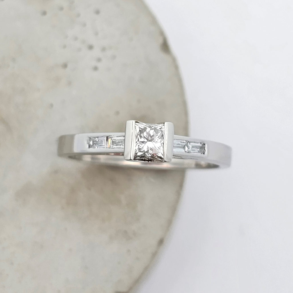 Platinum ladies engagement ring featuring an elevated semirub set princess cut diamond, stepping down to shoulders channels set with baguette diamonds. 