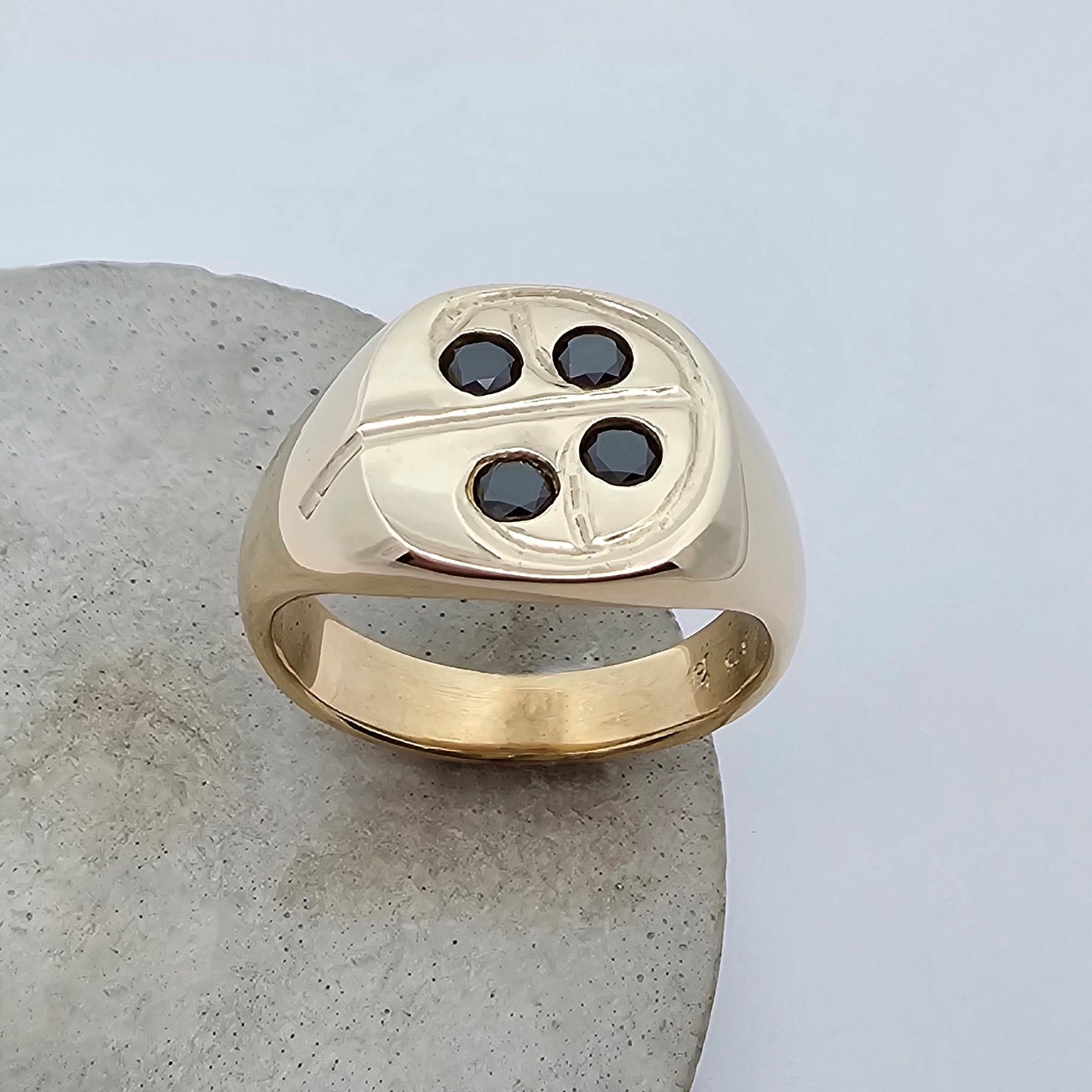 9ct yellow gold solid signet ring with a soft square shaped top set with four round black diamonds that are encased by an engraved koru pattern.