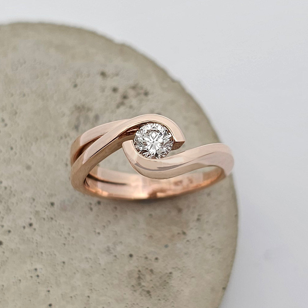 9ct rose gold ladies ring featuring a solitaire round white diamond in an asymmetrical crossover design.