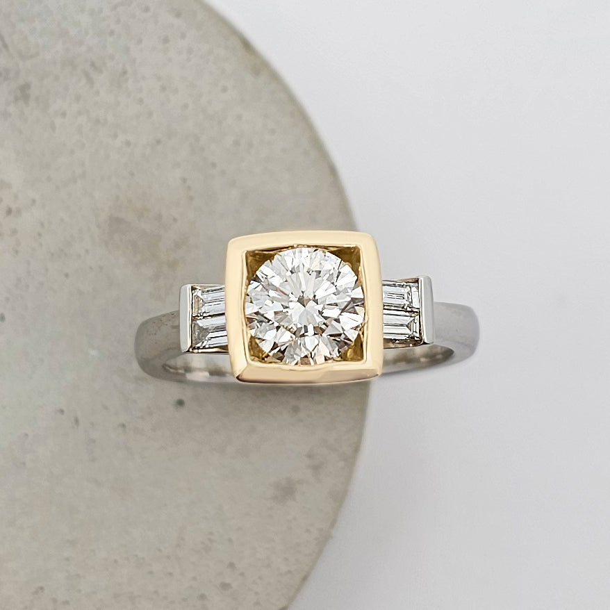 Platinum and 18ct yellow gold ring featuring a large sparkling round white diamond in a square yellow gold setting with channel set baguette white diamonds.