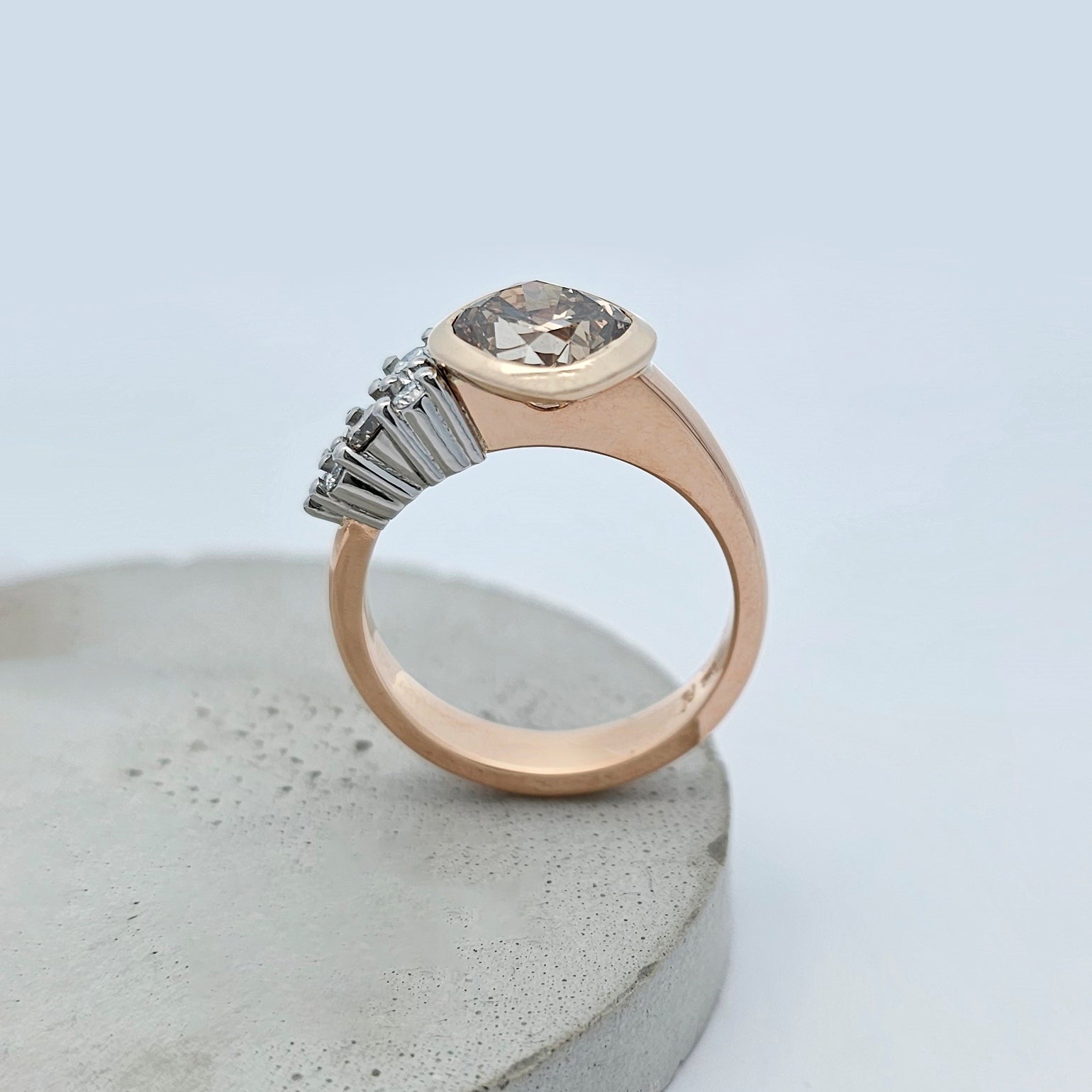 18ct rose gold and platinum ring featuring a large cushion shaped champagne diamond and asymmetrical claw set cluster of small round white diamonds.