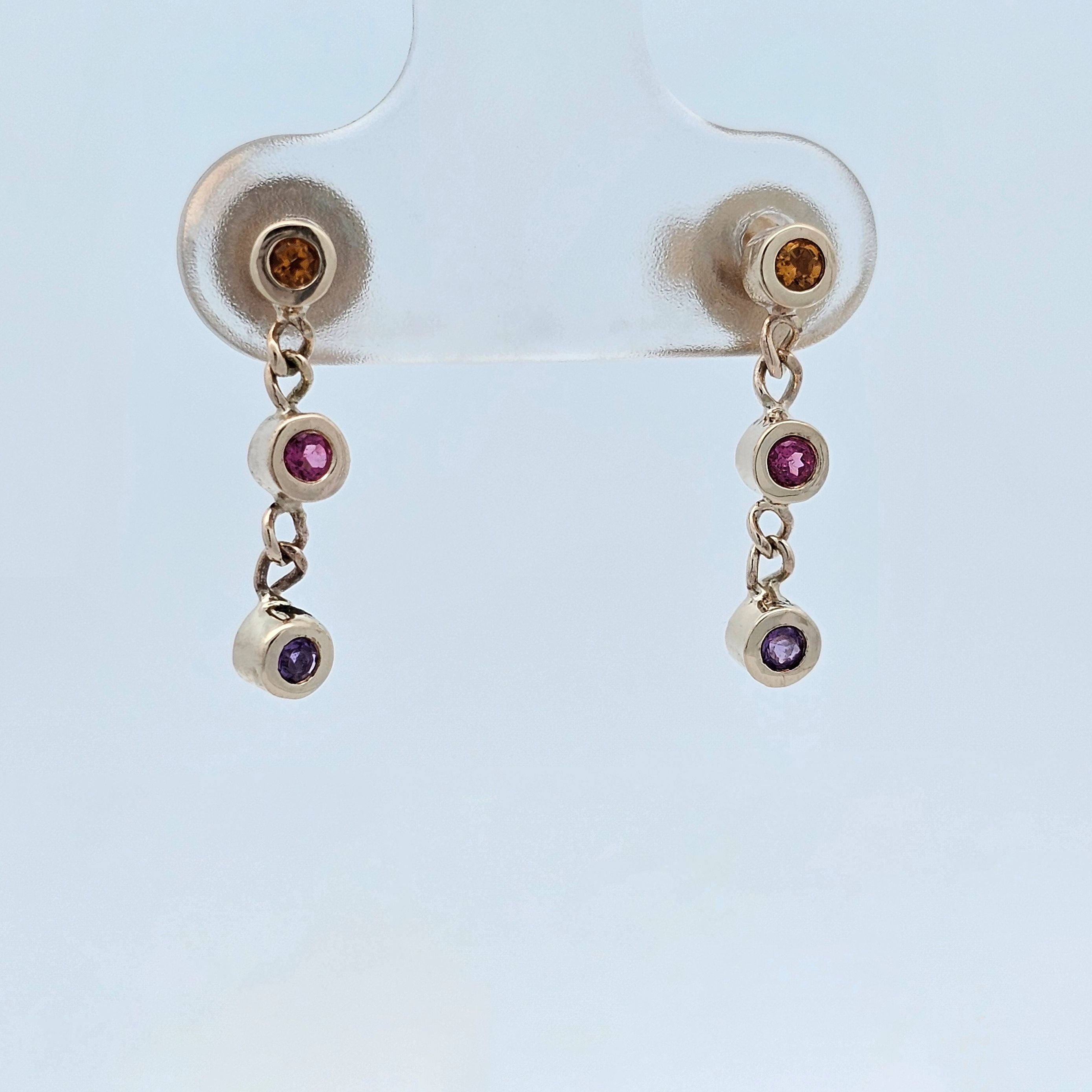Gold drop earrings with bezel-set gemstones in warm amber, pink and purple tones.