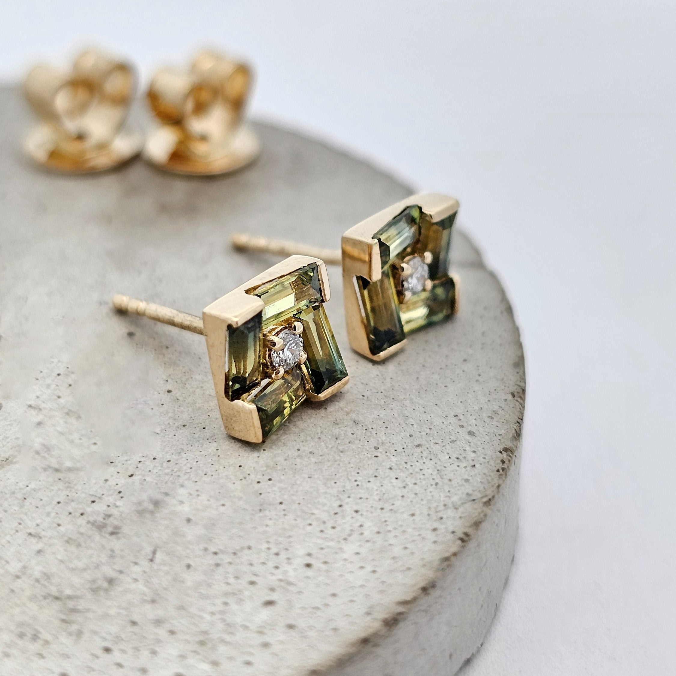 Yellow gold stud earrings featuring square-set green sapphires with diamond accents in a modern geometric design.