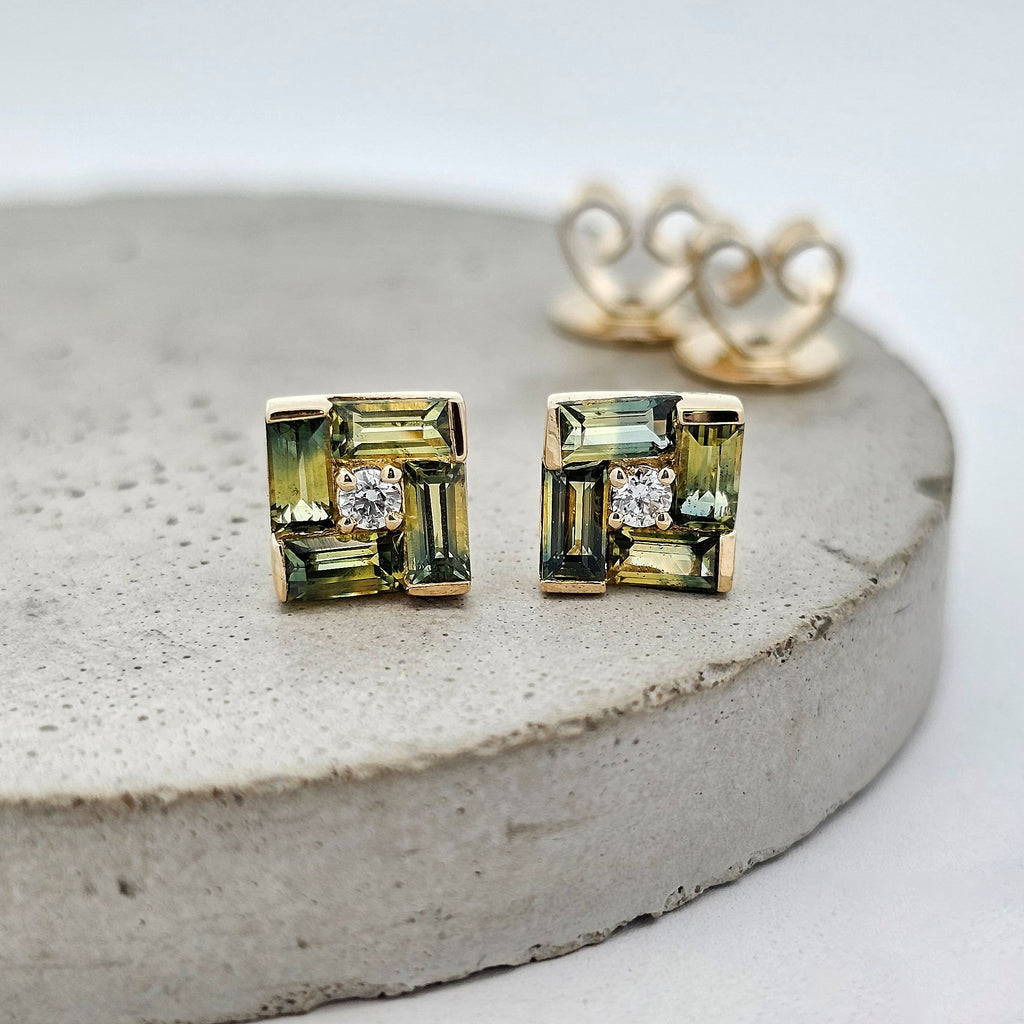 Yellow gold stud earrings featuring square-set green sapphires with diamond accents in a modern geometric design.