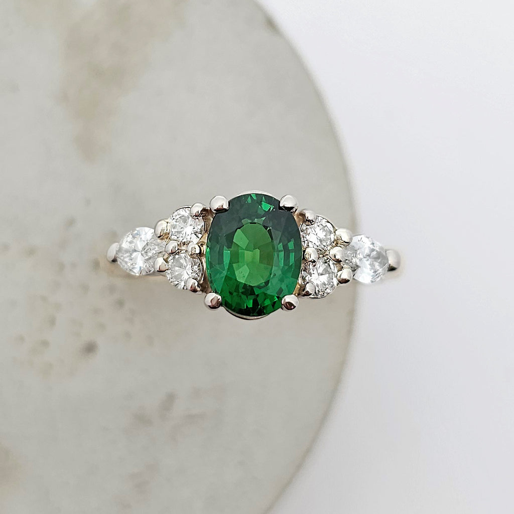 18ct yellow and white gold ladies ring with oval green tsavorite garnet claw set in the center and bright white round and marquise diamonds claw set in the shoulder.