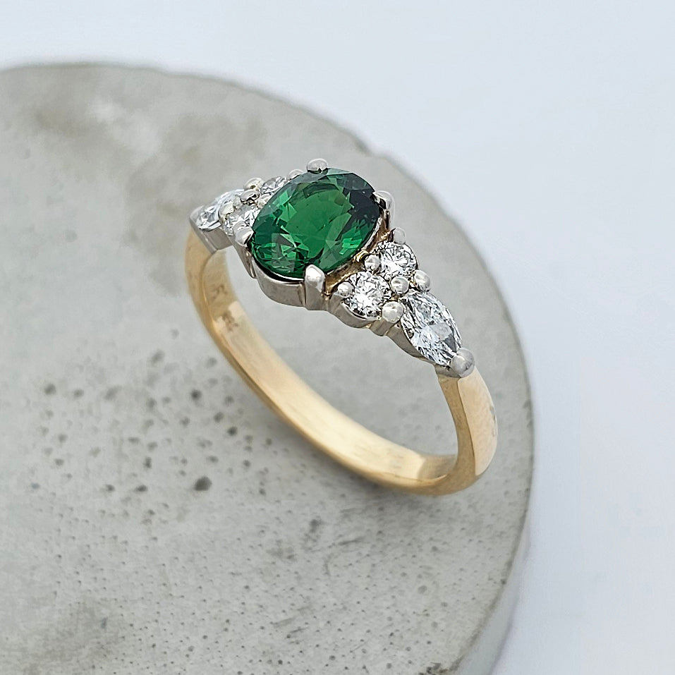 18ct yellow and white gold ladies ring with oval green tsavorite garnet claw set in the center and bright white round and marquise diamonds claw set in the shoulder.