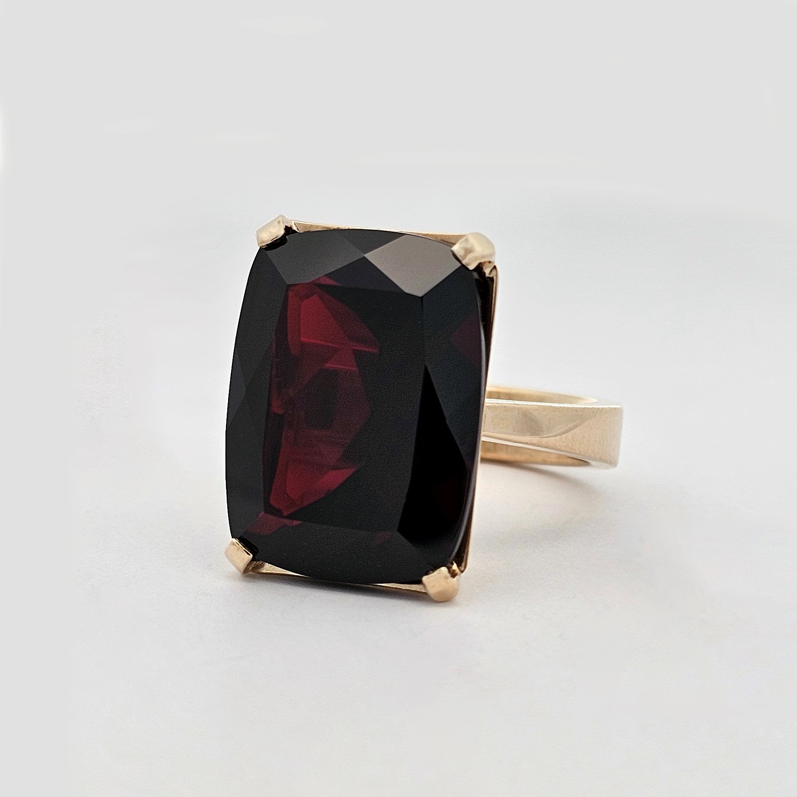 A simple 9ct yellow gold four claw setting holds an extra large, deep coloured elongated cushion cut garnet, with a square edged, solid yellow gold band.