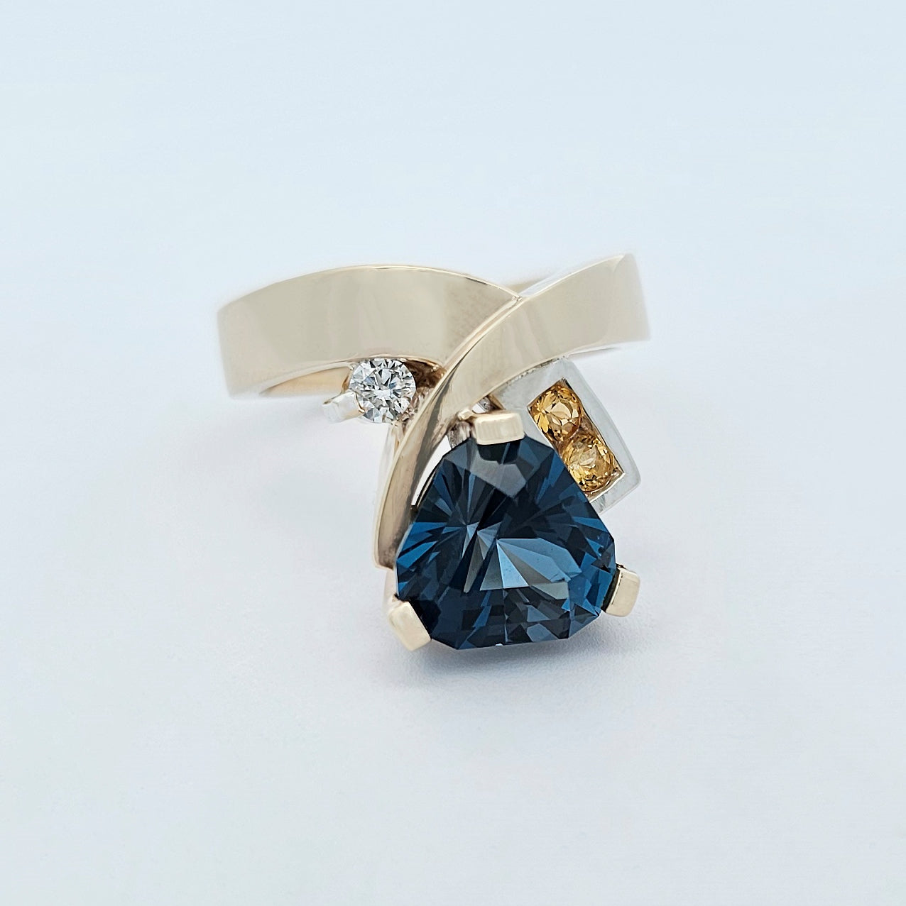 9ct yellow and white gold ladies dress ring with a trilliant cut blue topaz claw set, yellow citrine channel set in to one shoulder and a claw set bright white diamond.