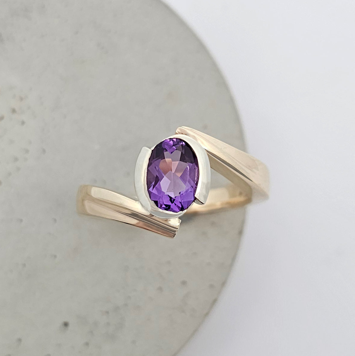 9ct yellow and white gold ladies dress ring with rub over set deep purple oval amethyst suspended between curved arms of yellow gold.