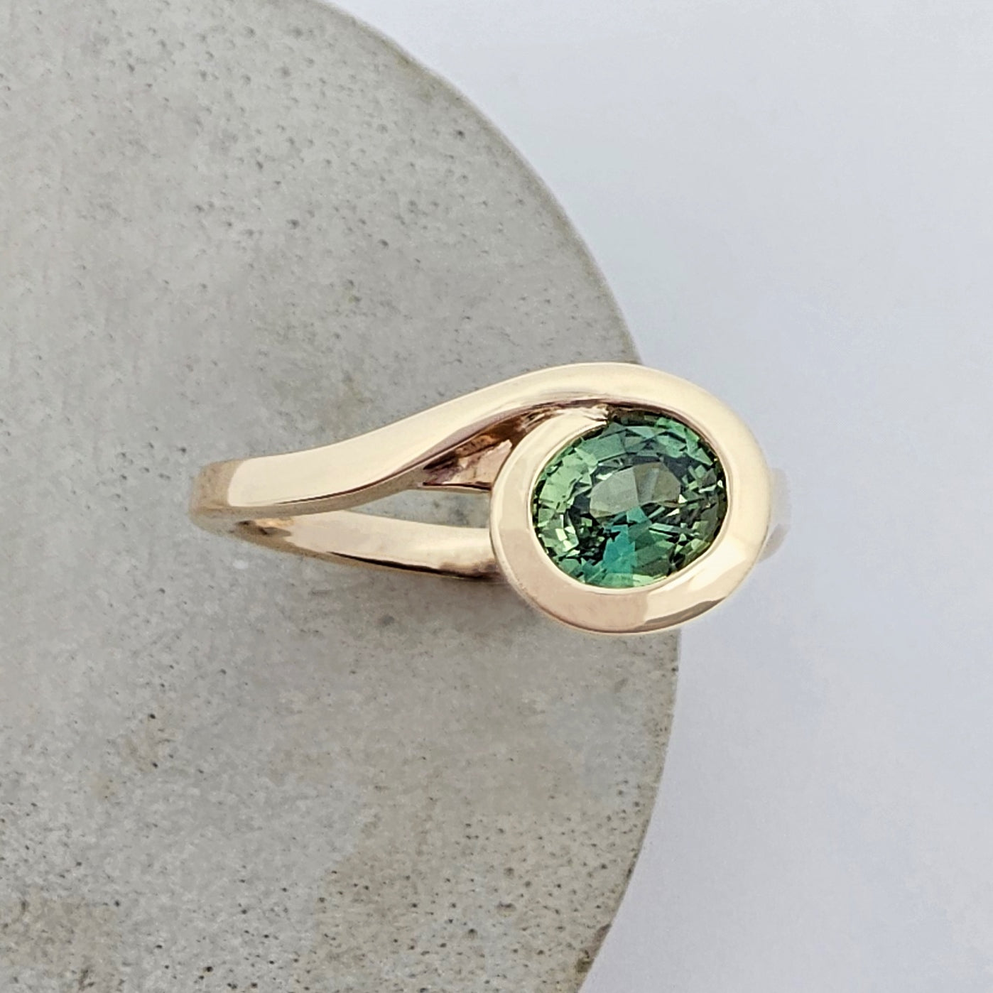 9ct yellow gold sweeps up from the band of this ring and swirls around a bright green yellow coloured oval sapphire in an asymmetric ring design.