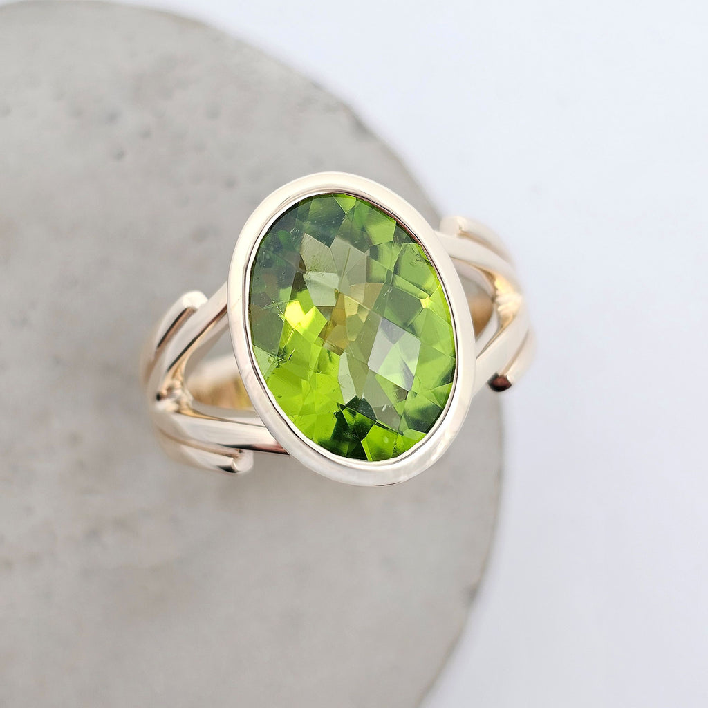 Enchanted oval checkerboard cut peridot ring in yellow gold with rub-over setting and split shoulders. Top View.