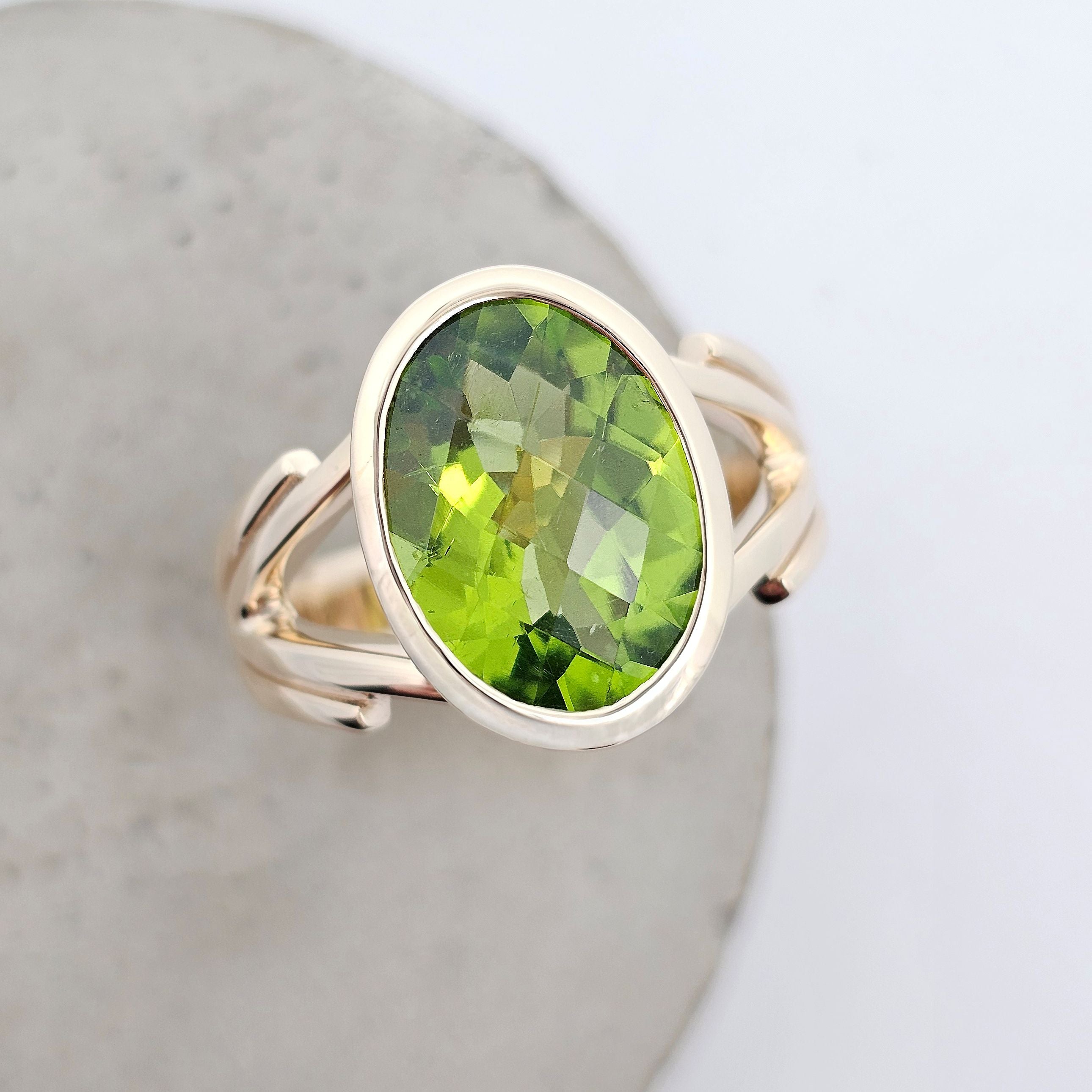 Enchanted oval checkerboard cut peridot ring in yellow gold with rub-over setting and split shoulders. Top View.