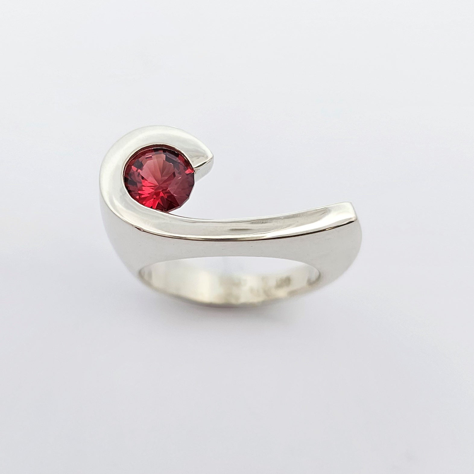 9ct white gold ladies dress ring featuring a deep red round shaped garnet set to the side of the finger in a solid curve of gold.