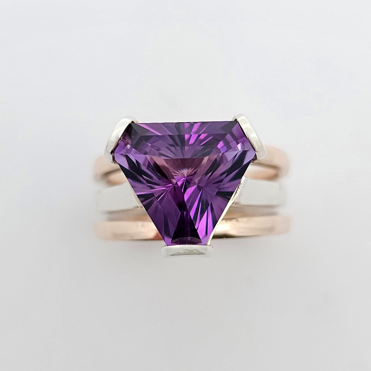9ct rose and white gold ladies dress ring  featuring a deep purple trilliant cut amethyst claw set above three bands of gold.