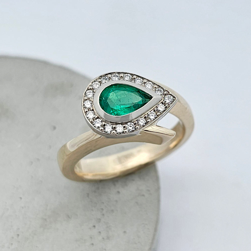 9ct yellow and white gold ladies ring with a rub over set pear shaped green emerald surrounded by a halo of bead set white diamonds in a cross over style band.