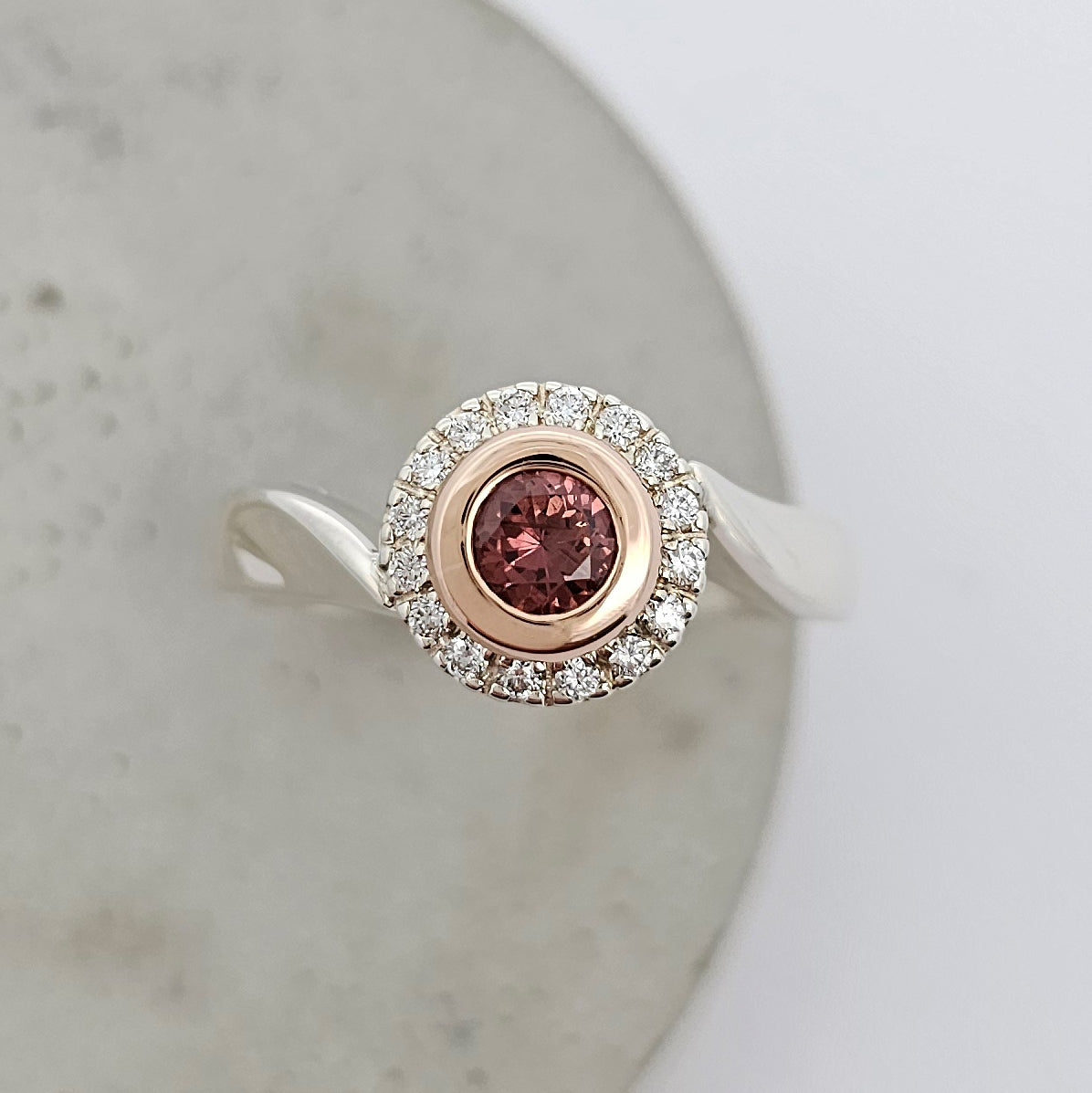 9ct white and rose gold ladies ring with a round pink brown sapphire surrounded by a halo of white diamonds and soft curved shoulders.