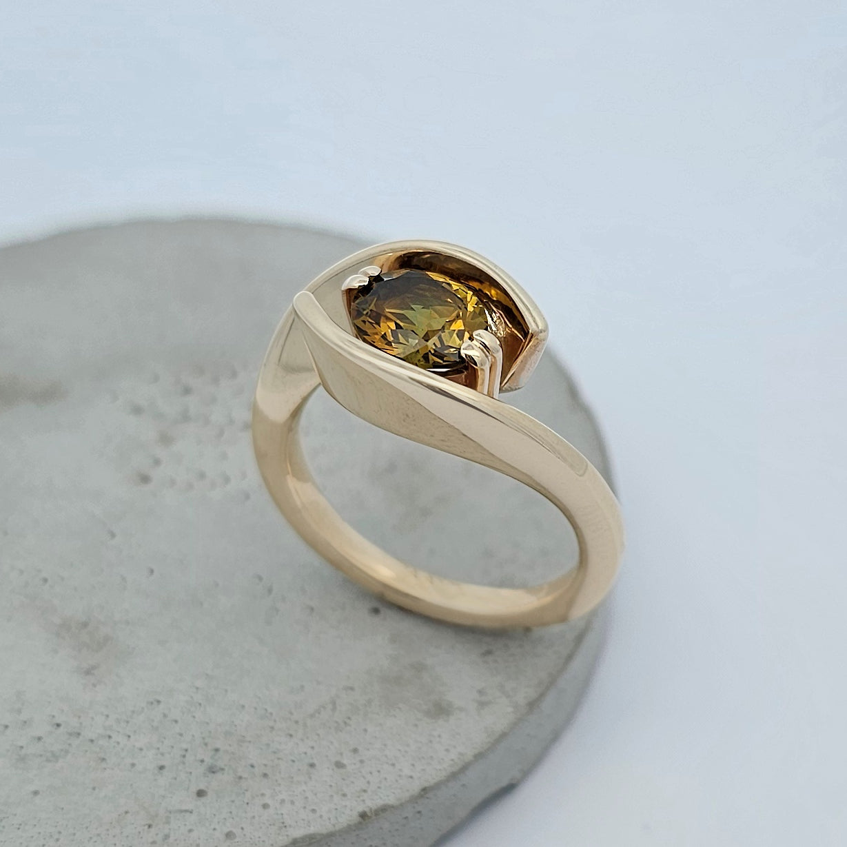 9ct yellow gold ring featuring sweeping solid gold shoulders curve up and around a claw set oval yellow green sapphire.
