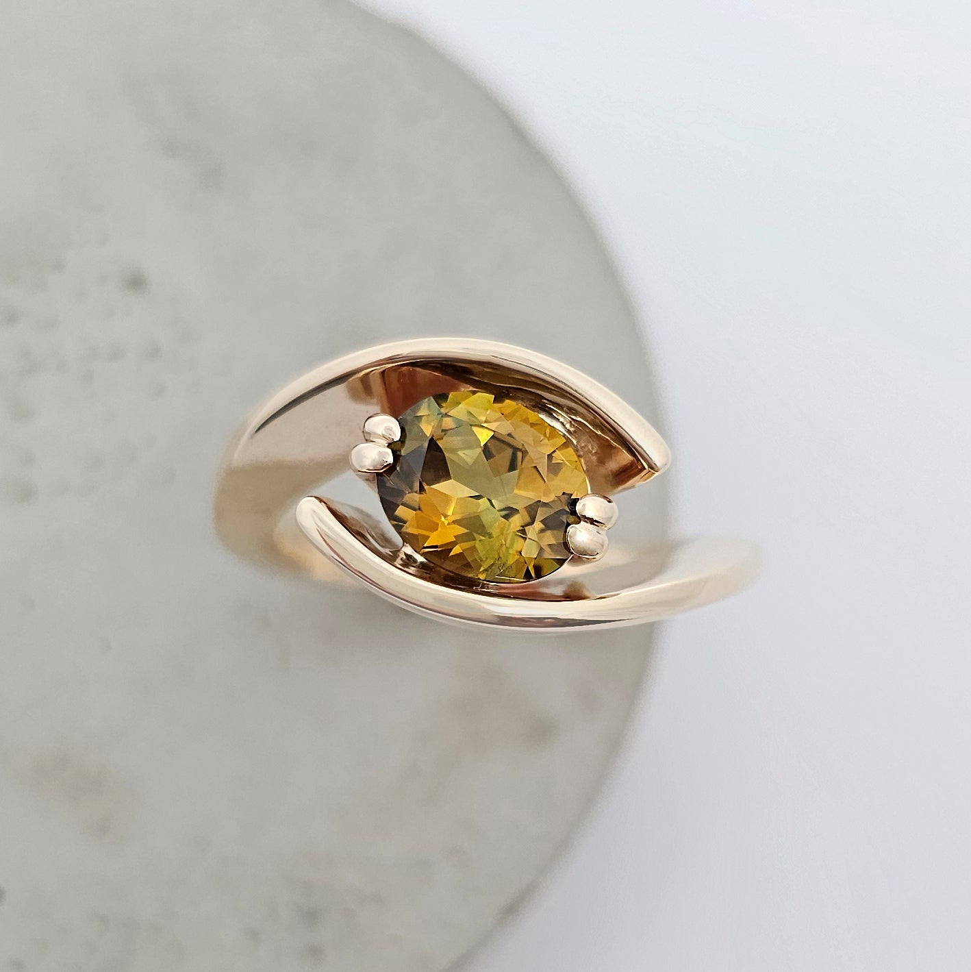 9ct yellow gold ring featuring sweeping solid gold shoulders curve up and around a claw set oval yellow green sapphire.