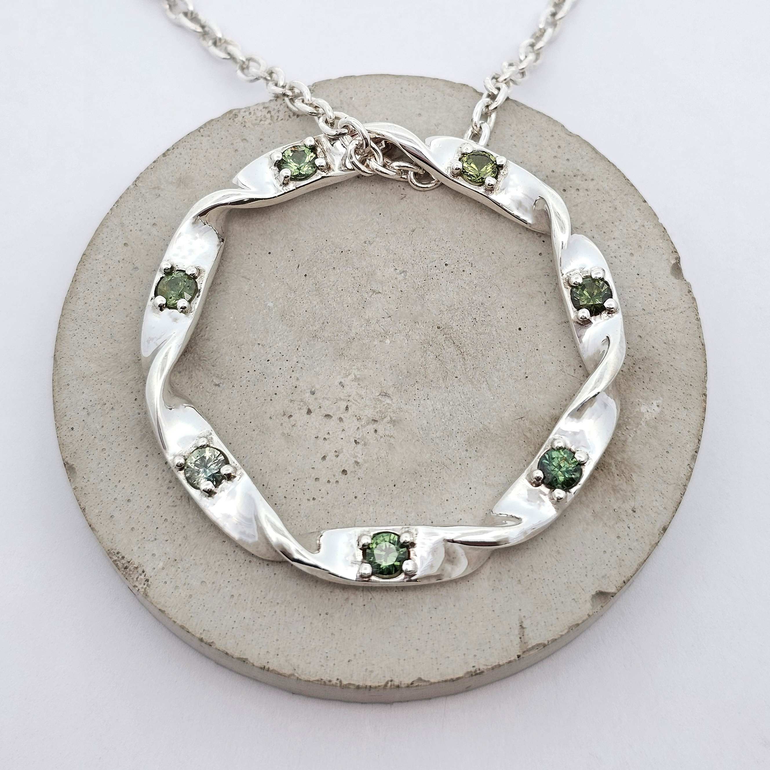 Sterling silver twist pendant set with round green sapphires along the curved design.