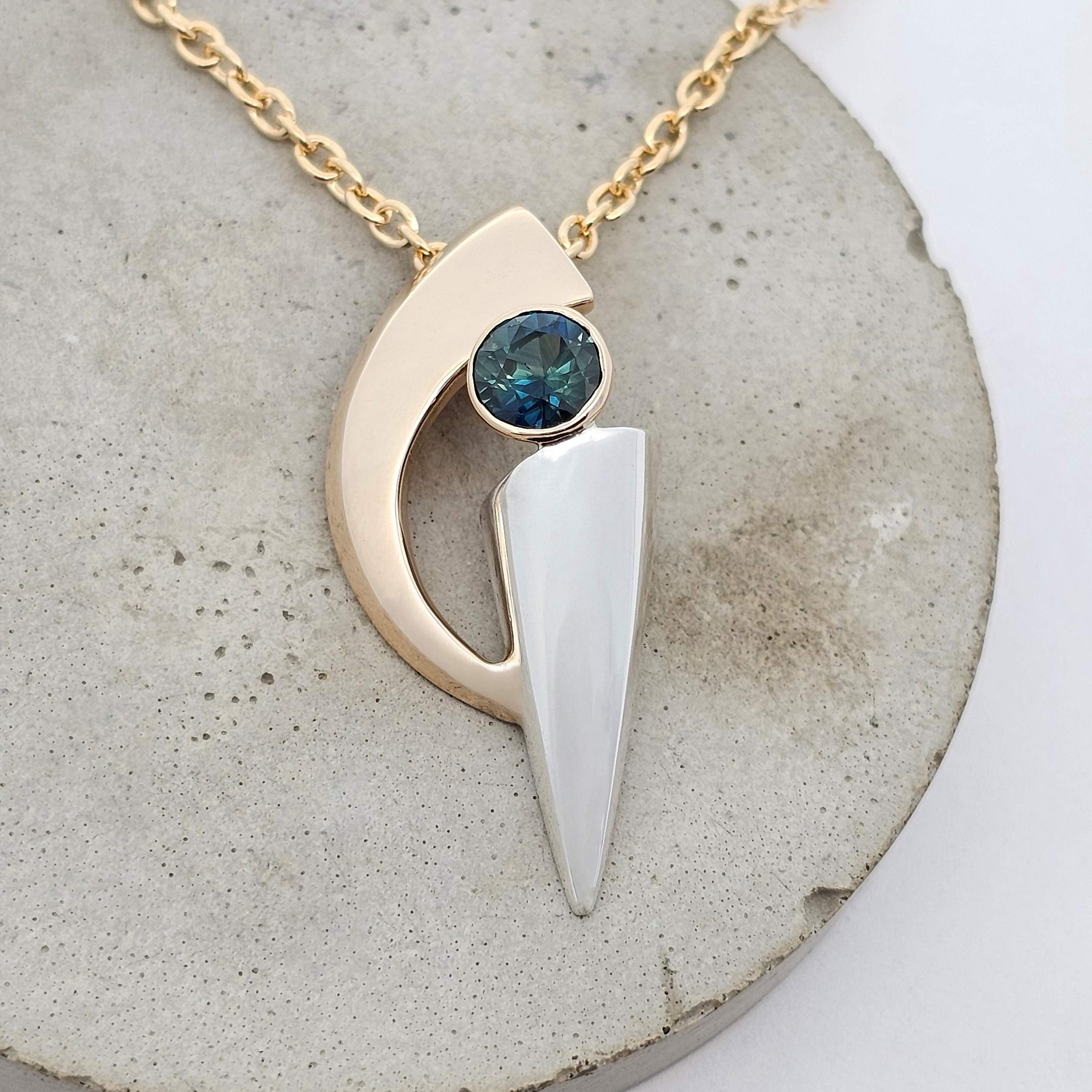 Blue-green sapphire pendant in yellow and white gold with a modern curved and pointed design.