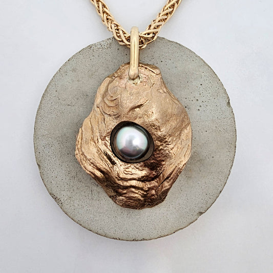 Golden Oyster pendant in solid yellow gold, cast from a natural oyster shell, featuring a lustrous dark grey-black pearl nestled within its organic form, hanging on a woven gold chain.