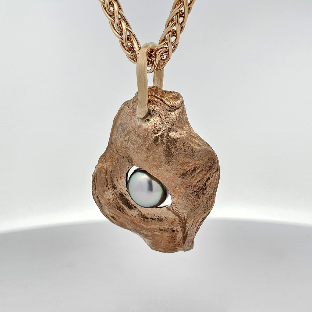 Golden Oyster pendant in solid yellow gold, cast from a natural oyster shell, featuring a lustrous dark grey-black pearl nestled within its organic form, hanging on a woven gold chain