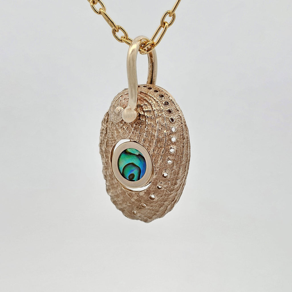 Pāua shell pendant cast in yellow gold featuring a central pāua pearl, with matte exterior and polished interior in an organic reversible design.