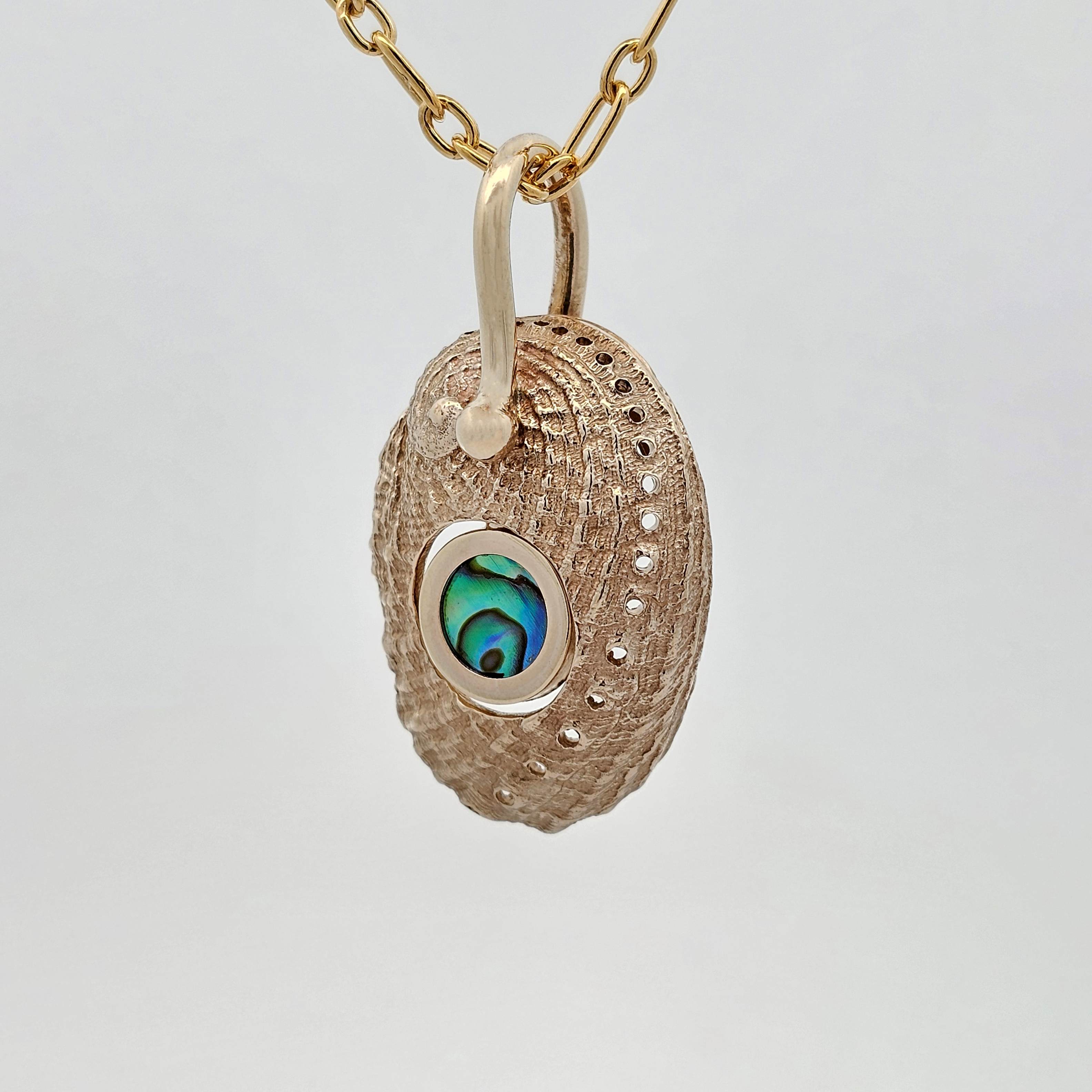 Pāua shell pendant cast in yellow gold featuring a central pāua pearl, with matte exterior and polished interior in an organic reversible design.