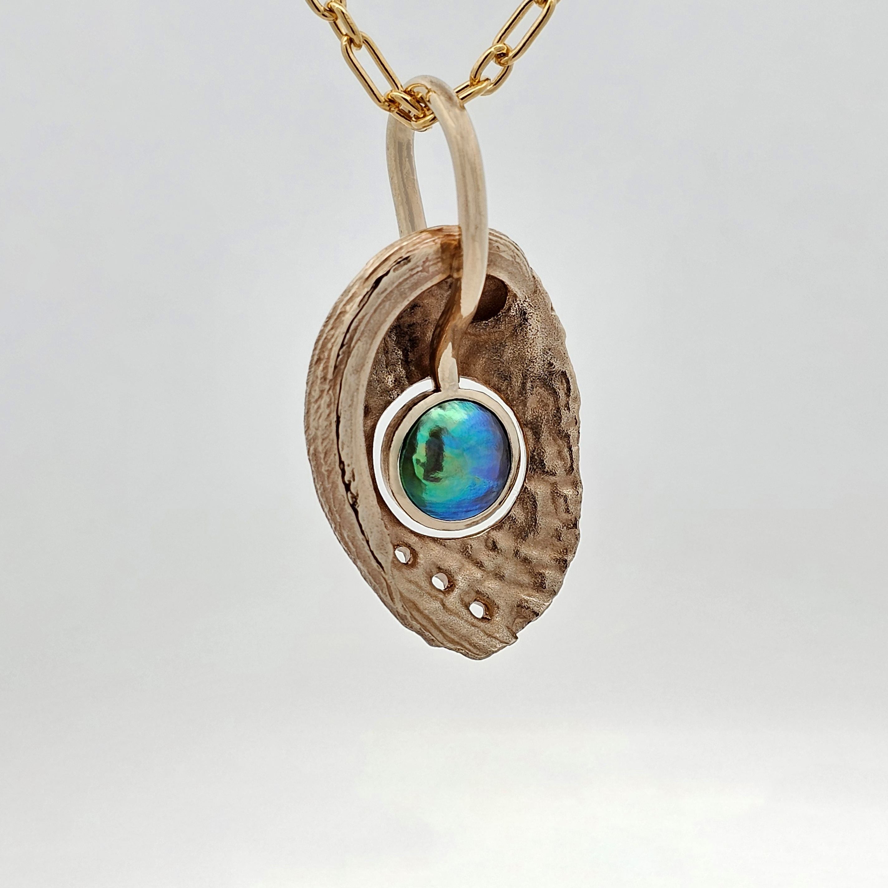 Pāua shell pendant cast in yellow gold featuring a central pāua pearl, with matte exterior and polished interior in an organic reversible design.