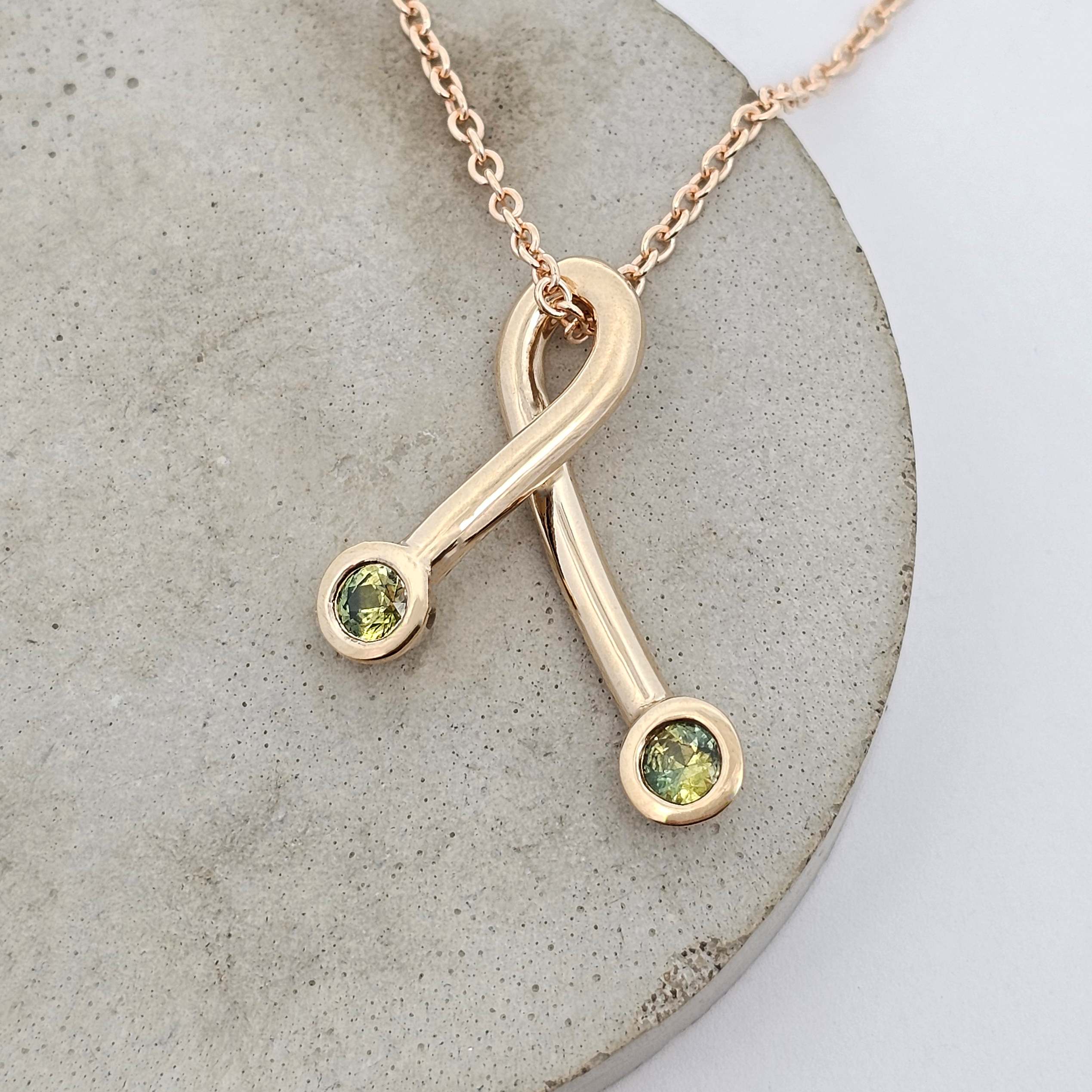 Yellow gold crossover pendant featuring two lemon-lime green sapphires at each end of the curved design.