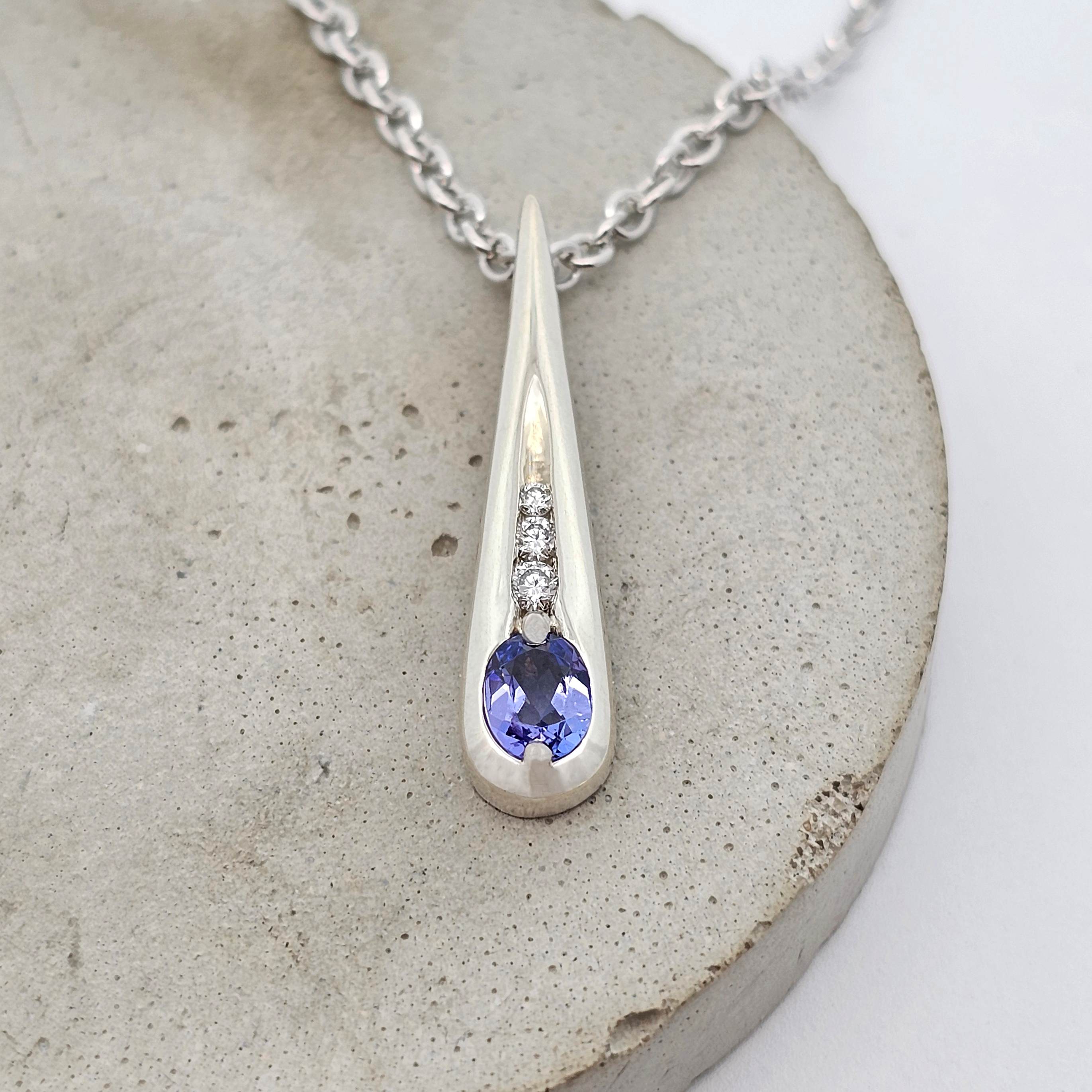 White gold drop pendant featuring a violet tanzanite and three small diamonds in an elongated design.