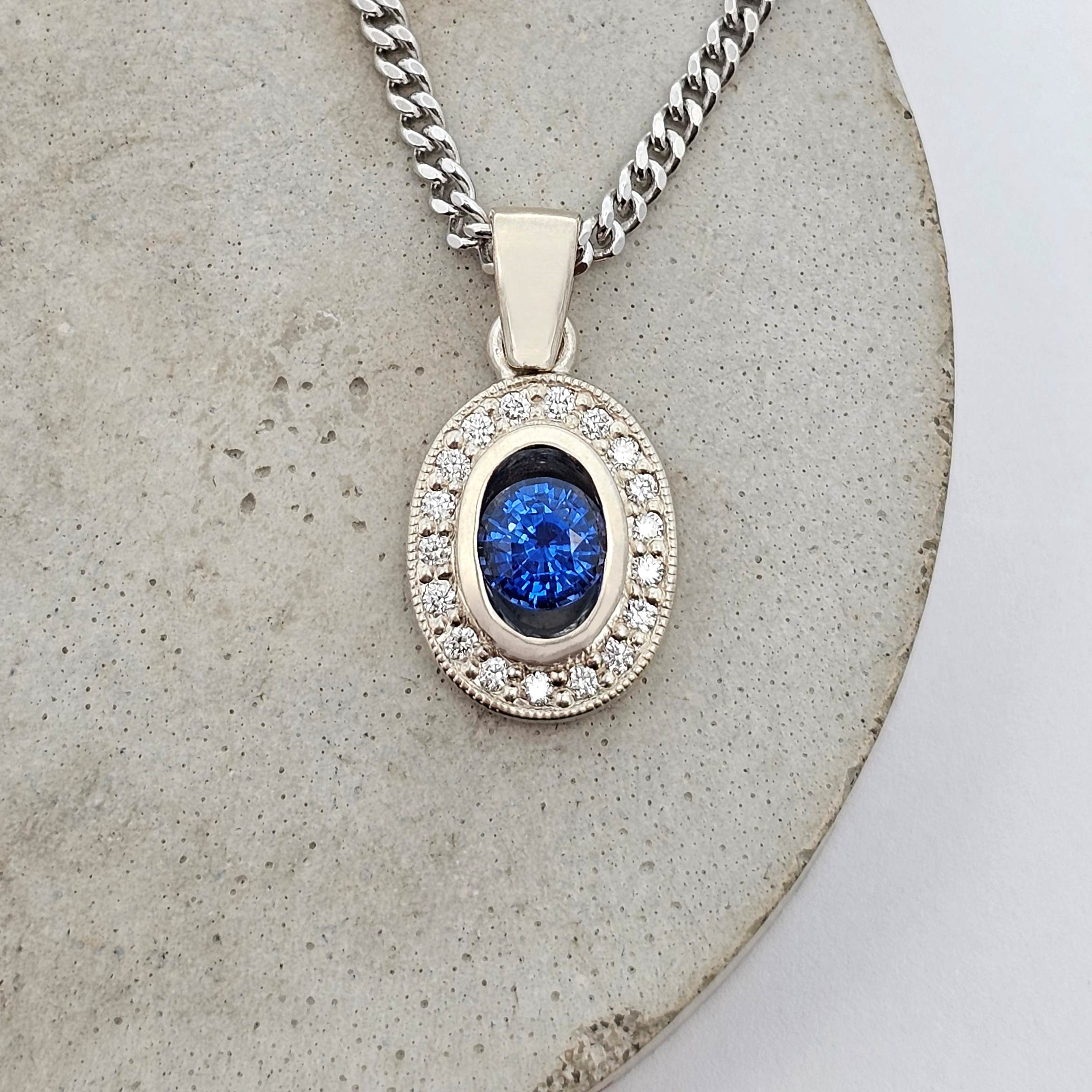 White gold halo pendant featuring a vivid blue Ceylon Sapphire surrounded by round brilliant diamonds.