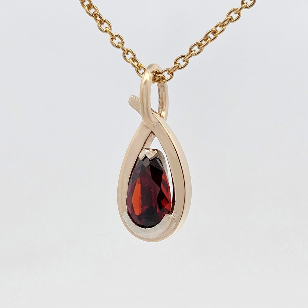African garnet pear pendant set in white gold with a sculptural yellow gold framework, handcrafted with a flowing modern design.