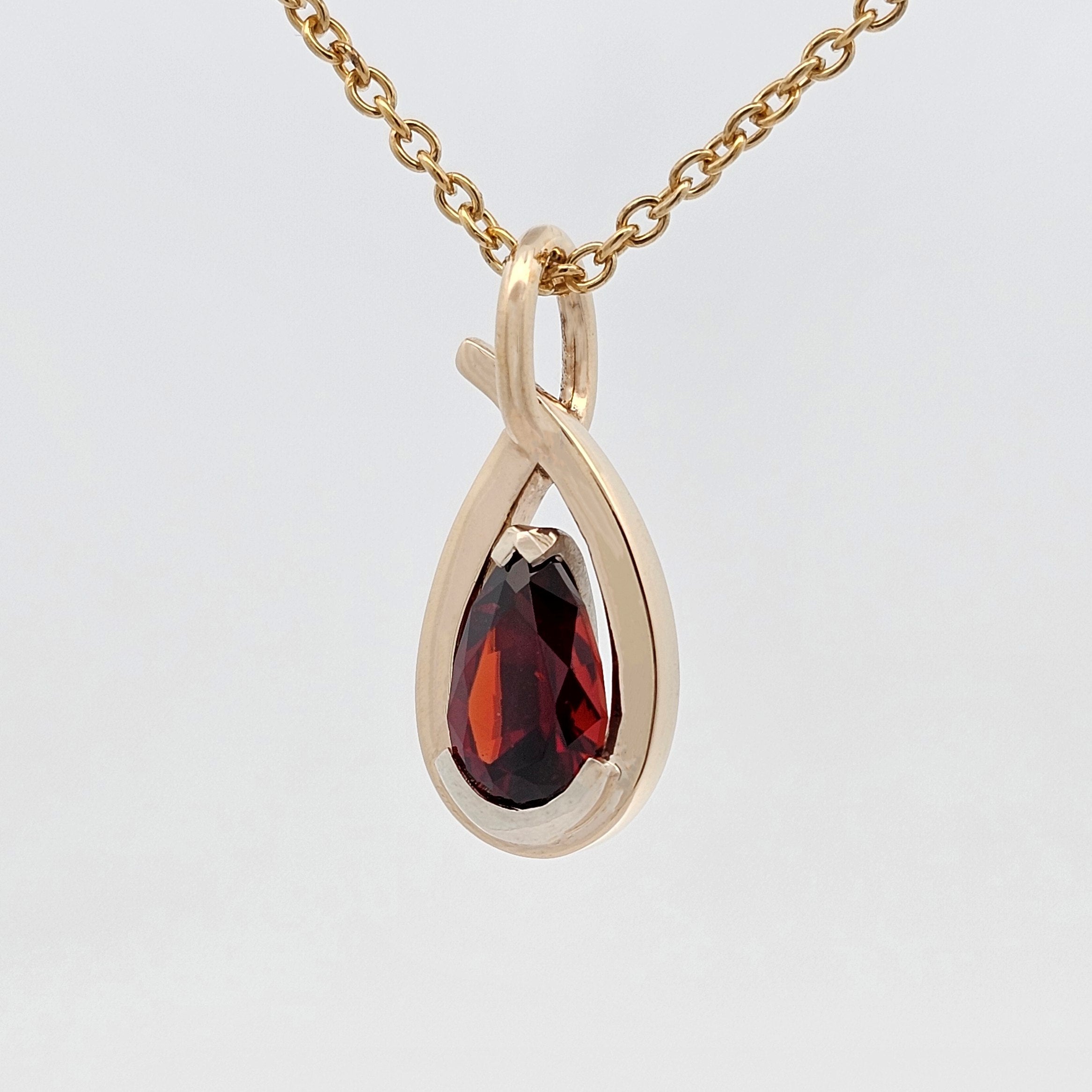 African garnet pear pendant set in white gold with a sculptural yellow gold framework, handcrafted with a flowing modern design.