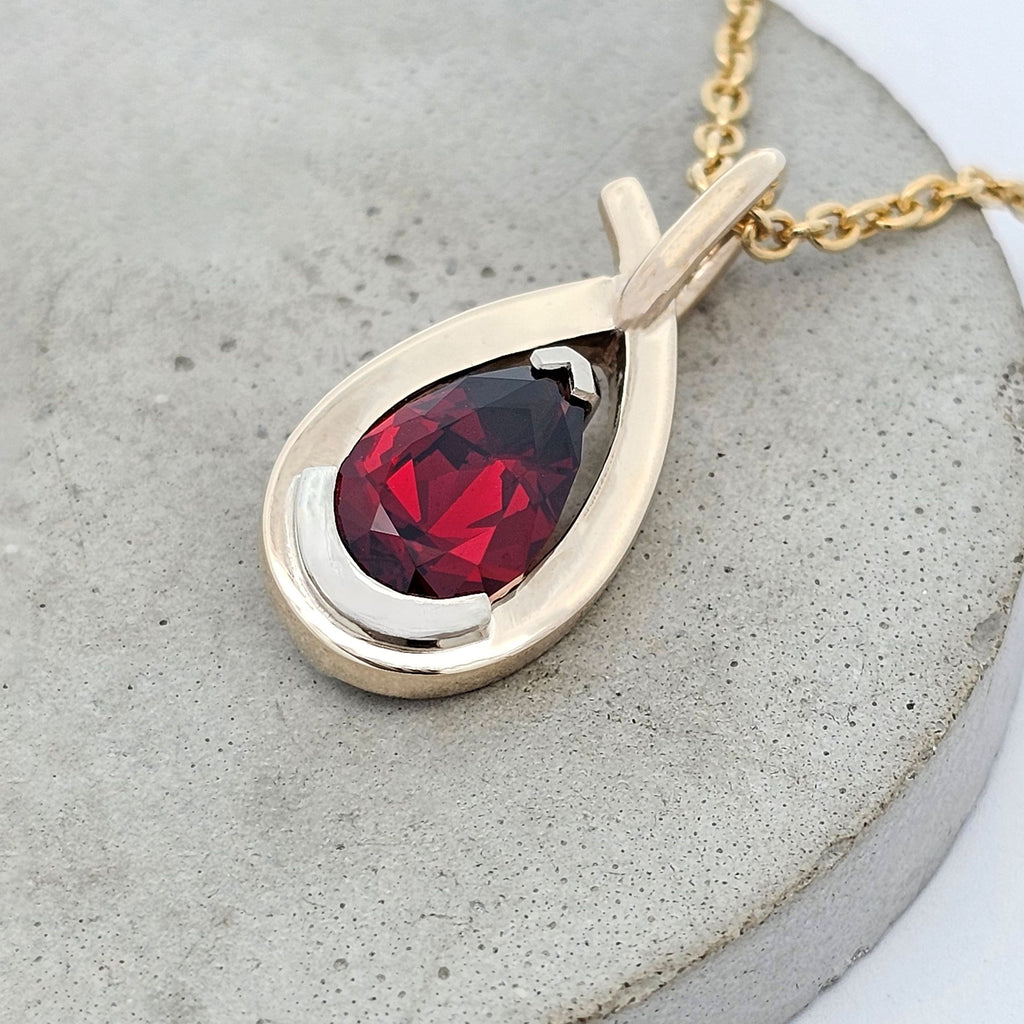 African garnet pear pendant set in white gold with a sculptural yellow gold framework, handcrafted with a flowing modern design.