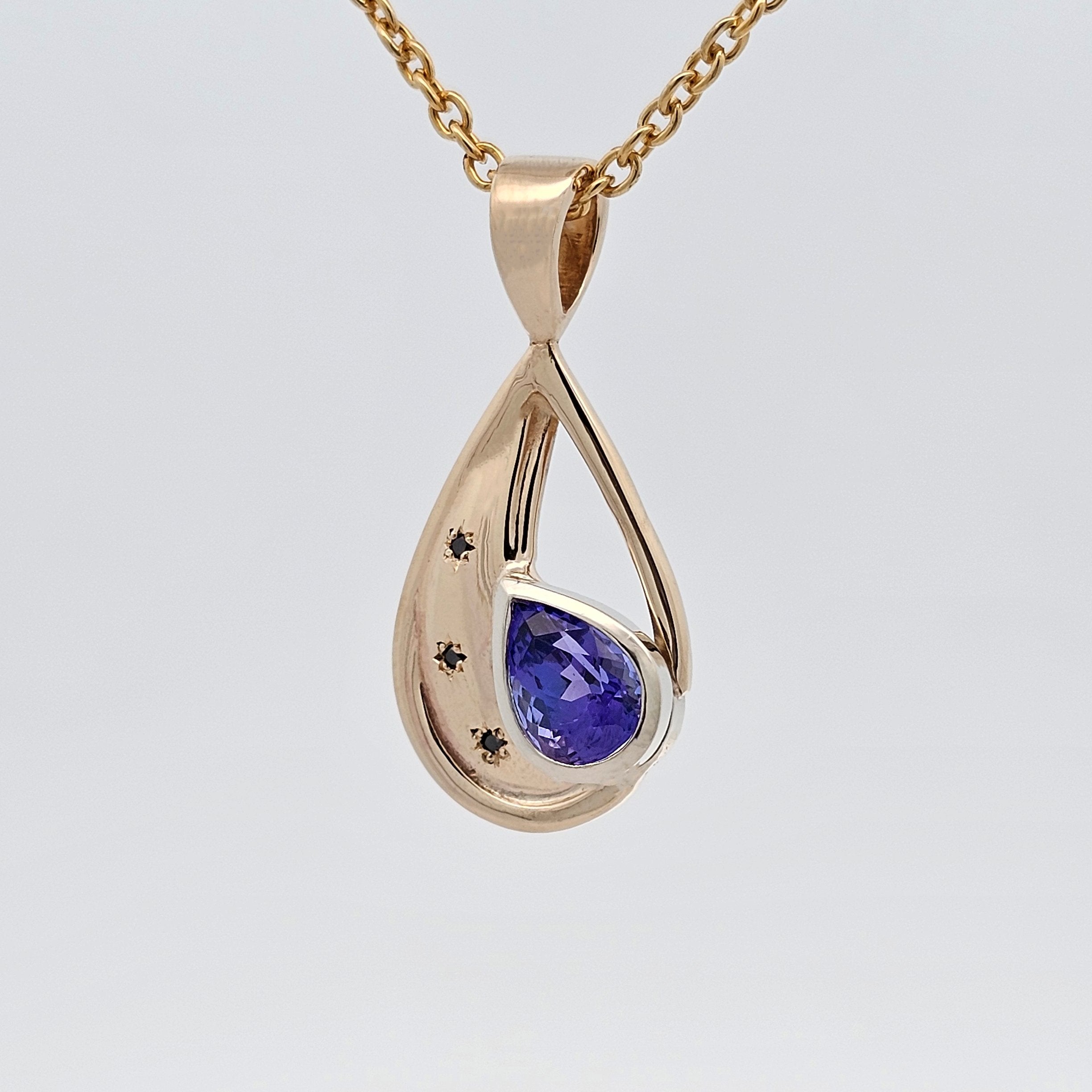 Gold pendant featuring a pear-cut tanzanite in a flowing design with star-set black diamonds, combining deep violet-blue tones with sculptural detail.