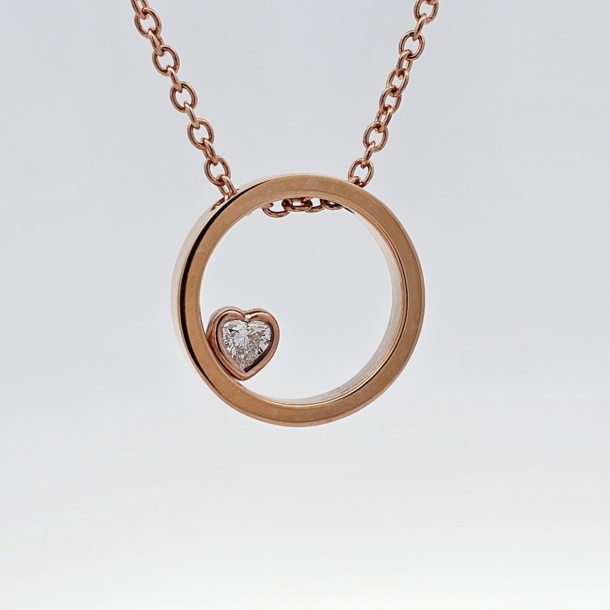 Rose gold open-circle pendant featuring a heart-shaped diamond at the base.