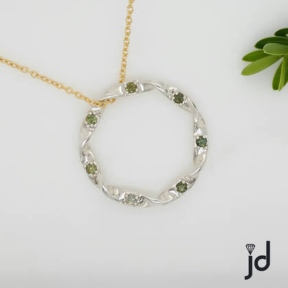 An extra large circle of twisted 9ct white gold creates an elegant pendant, set all the way around with 7 round green sapphires adding colour and texture. Suspended from a yellow gold cable chain.
